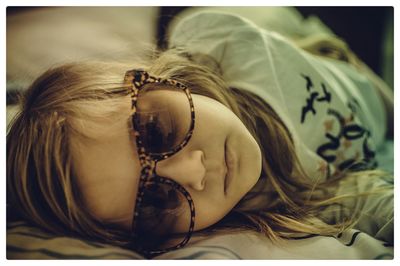 Close-up of girl wearing sunglasses lying on bed at home
