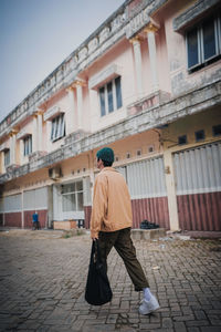Rear view of man walking on street against building