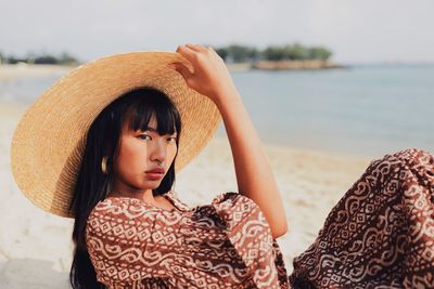 Portrait of young woman wearing hat sitting at beach