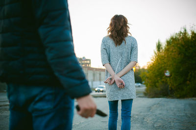 Rear view of man holding knife in front of woman with tied hands
