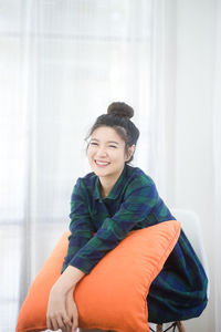 Portrait of smiling young woman sitting with pillow at home