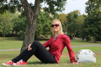 Full length of woman wearing sunglasses sitting on grassy field at park