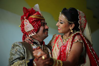 Smiling bride and groom with holding hands against wall at home