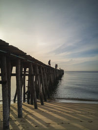 Wooden pier on beach against sky during sunset