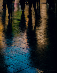 Low section of people walking on wet street with color reflections