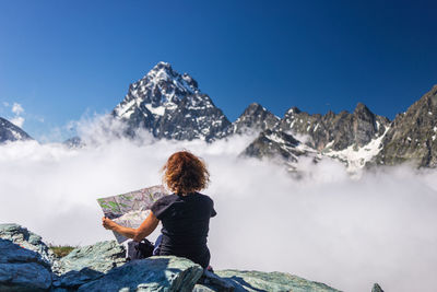 Rear view of man looking at snowcapped mountain against blue sky