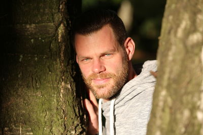 Portrait of young man against tree trunk