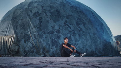 Portrait of man sitting on rock against sky