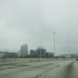 Road by buildings against sky in city