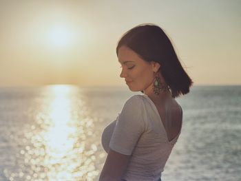 Side view of sensuous young woman against sea during sunset