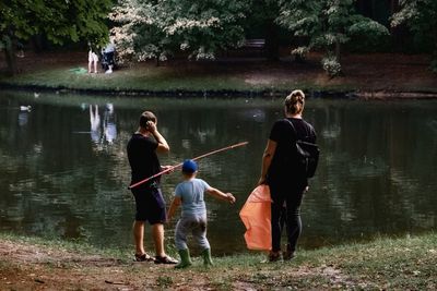 People standing by lake against trees