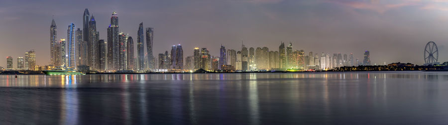 Illuminated modern buildings by city against sky