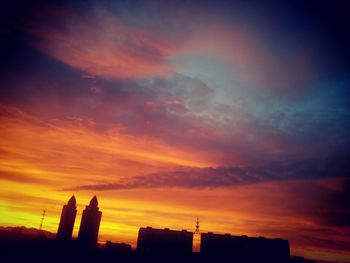 Silhouette of city against cloudy sky during sunset