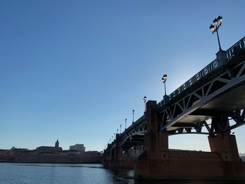 Bridge over river in city against clear blue sky