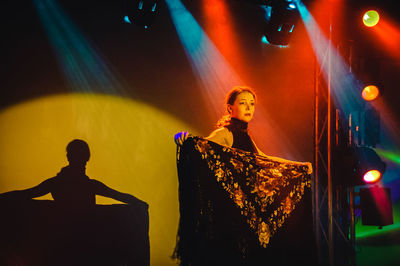 Full length of young woman standing against illuminated wall