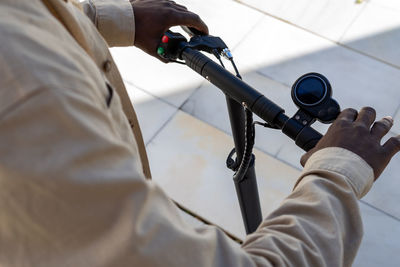 High angle of crop unrecognizable ethnic male standing on modern electric scooter while using gas and break on handlebar