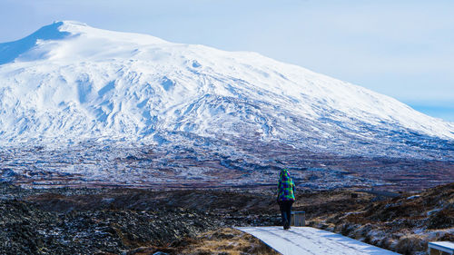 Rear view of man standing on snowcapped mountain against sky