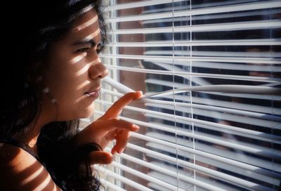 Close-up of woman looking though window blinds