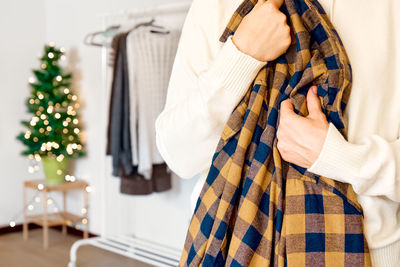 Woman's hands holding warm plaid shirt in the clothes shop with blurred christmas tree background.