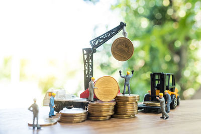 Close-up of figurines with toy crane and forklift with coins on table