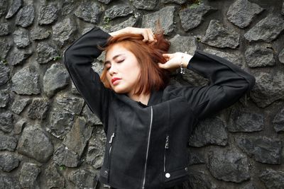 Woman with closed eyes standing against stone wall