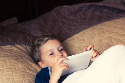 Portrait of boy using digital tablet while lying on bed at home