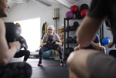 Senior woman with kettlebell exercising amidst people at health club