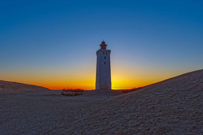 Lighthouse by sea against clear sky