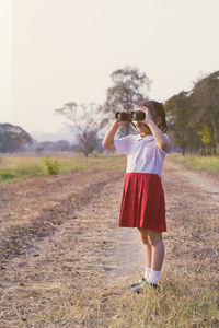 Full length of girl in school uniform looking through binoculars while standing at field