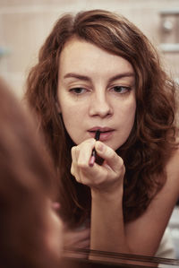 Woman paint her lips with lipstick in front of mirror,