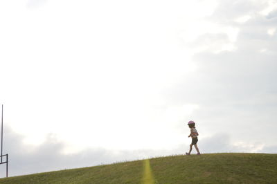 Side view of girl walking on grassy field against sky