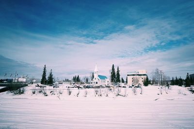 Houses on snow covered field against cloudy sky