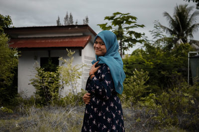 Woman standing by building against trees and house