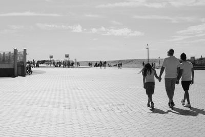 Rear view of people walking on sea in city against sky