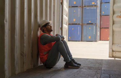 Side view of young man looking away while sitting on wall