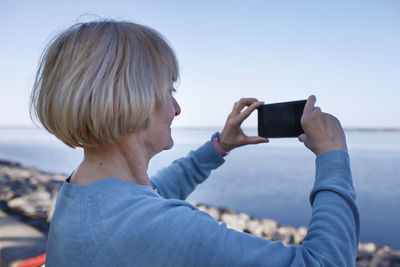 Woman photographing with mobile phone against sky