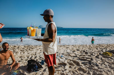 Rear view of shirtless man standing on beach against sky