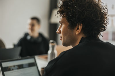 Rear view of curly haired young male computer programmer looking away