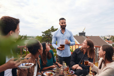 Man talking with friends while holding drink on terrace