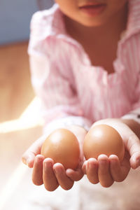Midsection of girl holding brown eggs while sitting at home