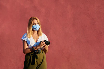 Young woman with a mask and a camera on a red background