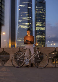 Businessman with bicycle using smart phone by wall at night