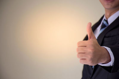 Midsection of businessman gesturing thumbs up against beige background