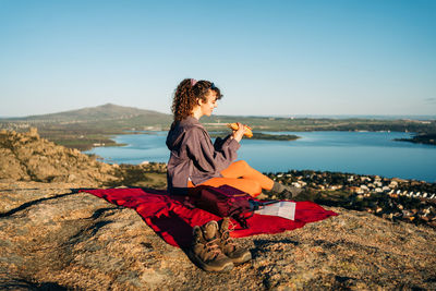 Woman sitting on rock at beach against clear sky