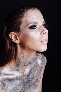 Close-up young woman with silver bodypaint over black background
