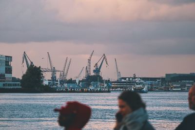 Rear view of cranes at harbor against cloudy sky