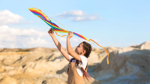 A girl in a summer dress launches a kite into the sky in the wild.