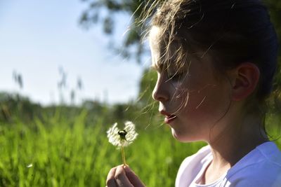 Close-up side view of girl blowing dandelion on land