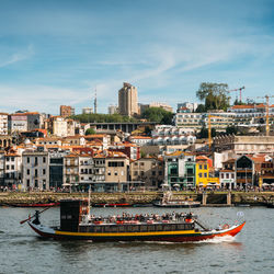 Boats in river by buildings in city against sky