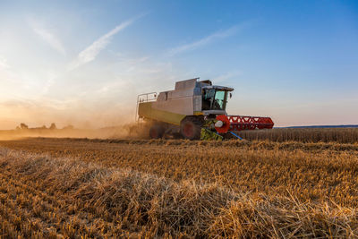 Tractor harvesting on agricultural field against sky